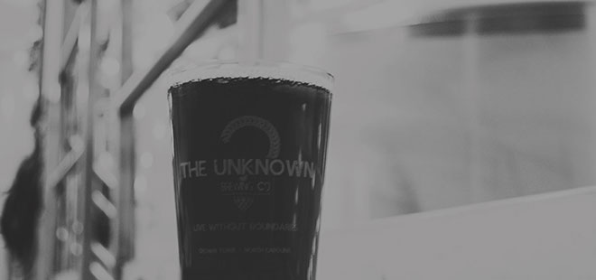 Black and white photo of a pint glass of beer in an industrial setting.