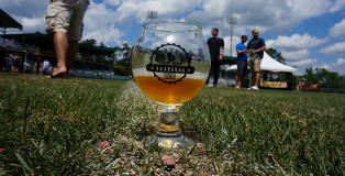 Augusta Beer Fest glass sitting on grass with a blue cloudy sky overhead