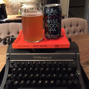 Wild Heaven Wise Blood IPA can and glass atop orange O'Connor novel on top of black typewriter