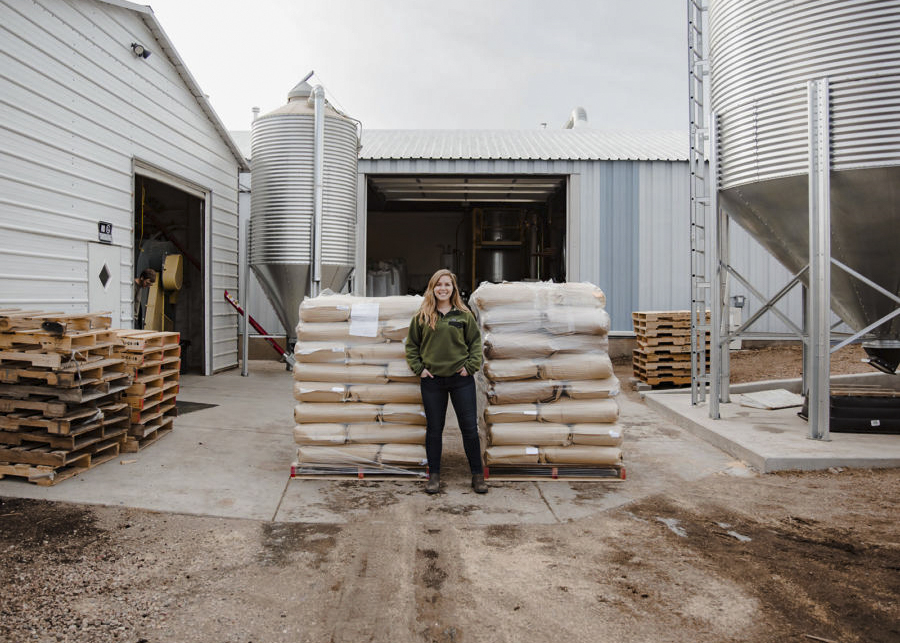 Twila Soles stands in front of pallets of gluten free beer malts near silos outside her malting facility