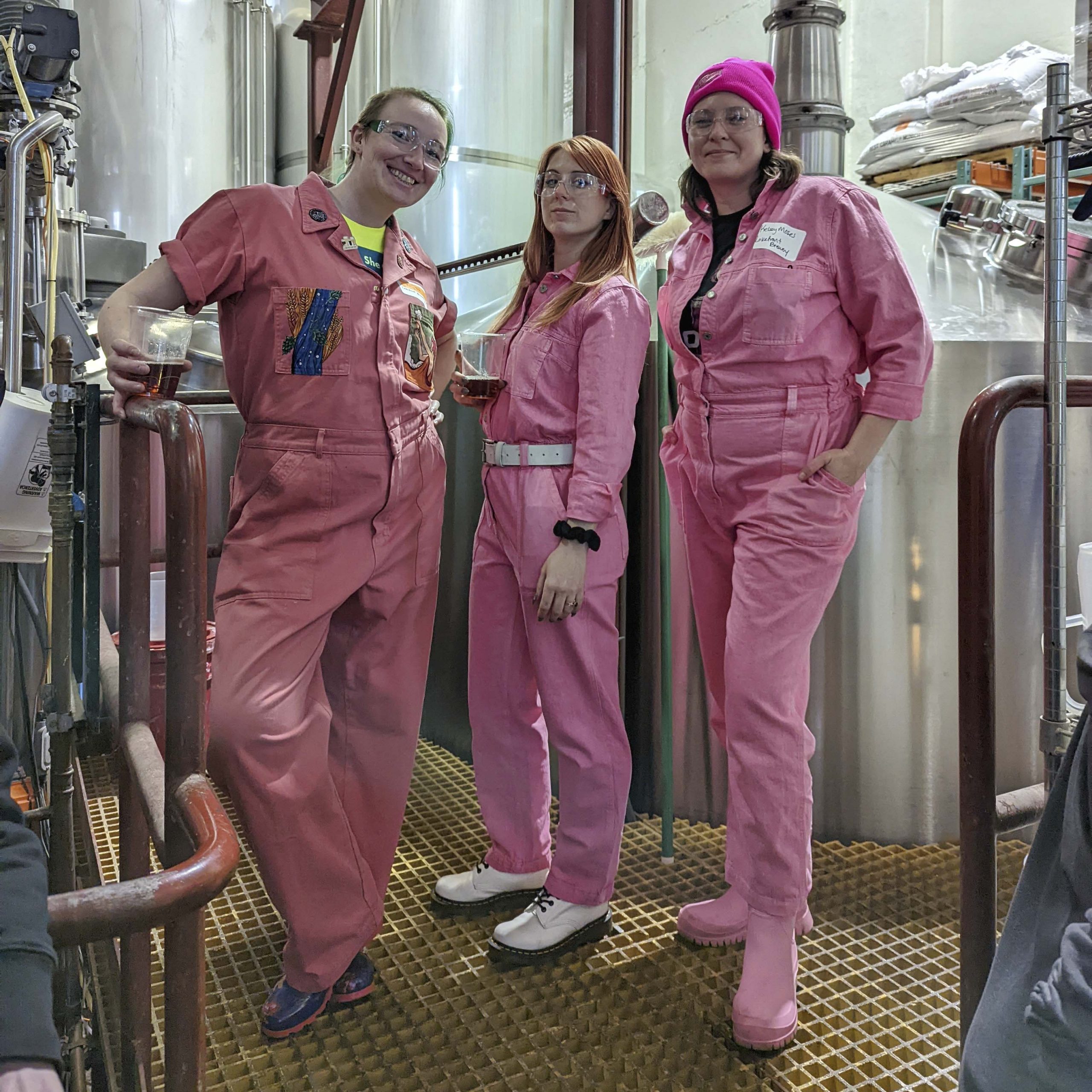 Three women in pink coveralls stand on the brew deck at Lakefront Brewery