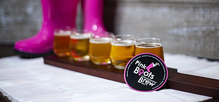 A flight of five beers sits in front of a pair of hot pink boots, and a magnet with the Pink Boots Society Collaboration Brew Day logo