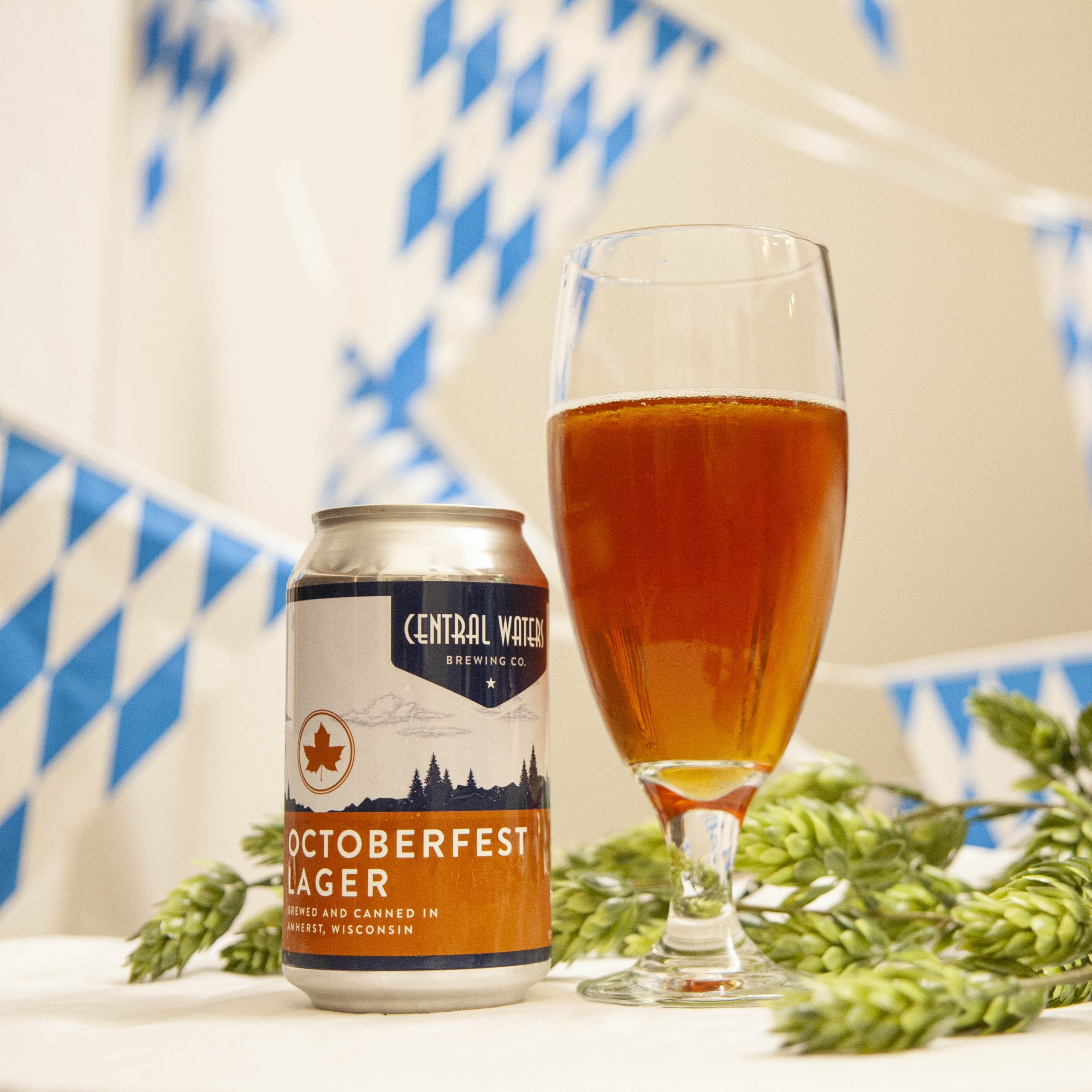 Central Waters' Octoberfest Lager is poured into a chalice glass, amidst hop cones and decorative blue and white bunting.