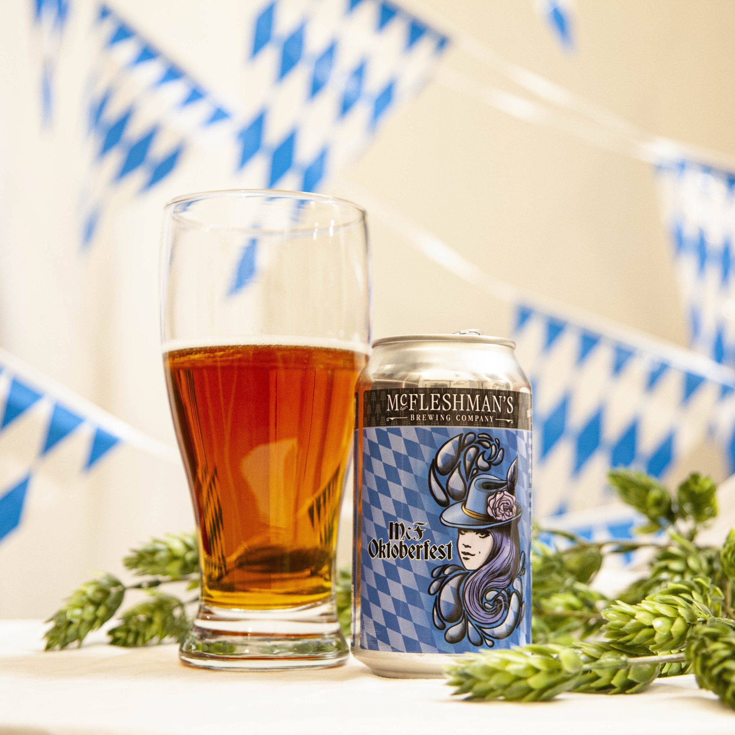 McFleshman's Oktoberfest is poured into a pilsner glass, amidst hop cones and white and blue bunting. 