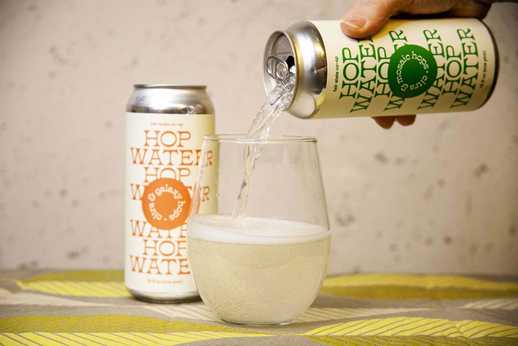 A can of Fair Stat Co-op Hop Water is poured into a stemless wineglass. 