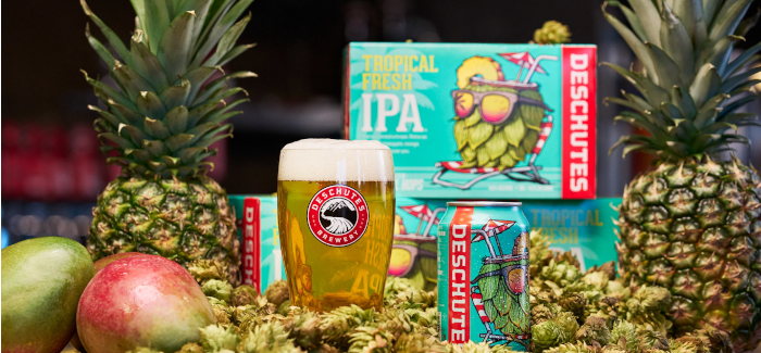 A glass of golden beer and a can in front of a six-pack box of Deschutes Brewery's Tropical Fresh IPA, surrounded by fresh pineapple and mango.