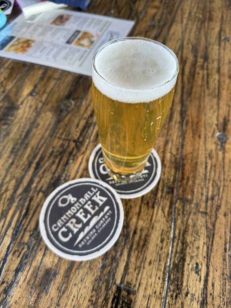 A photo of beer in a stylized Pilsner glass, photographed from above with a half-inch head on a Cannonball Creek coaster. A menu is in the background.