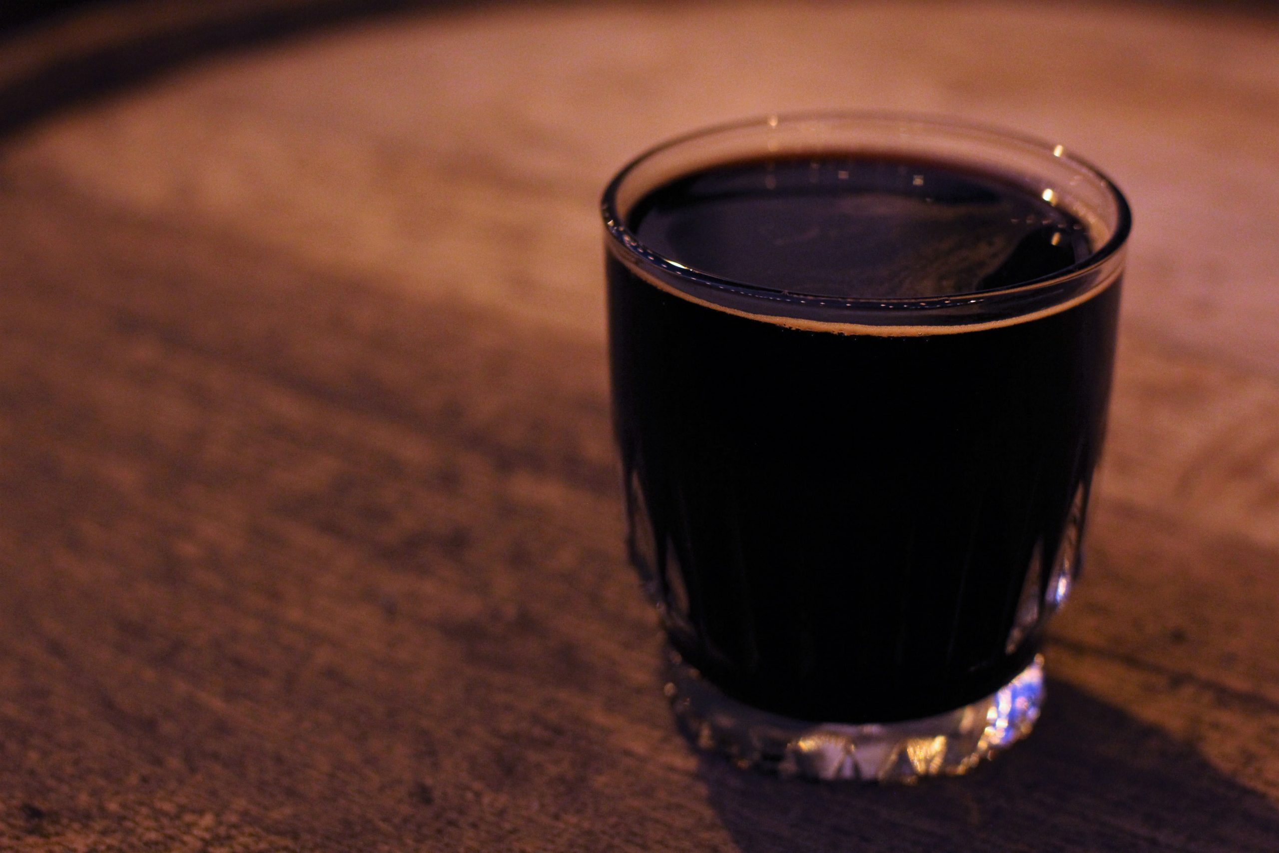 A moody photo of a dark beer in an old fashioned glass on a wood tabletop.