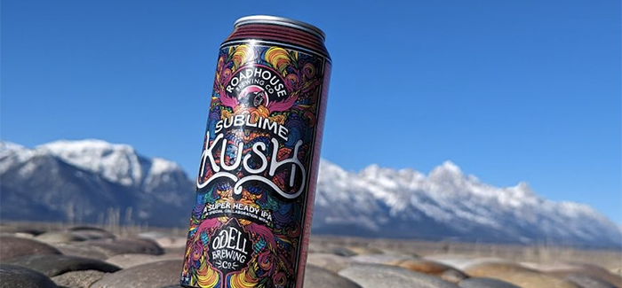 A brightly illustrated beer can on a cairn of rocks with a mountain range and blue sky in the background